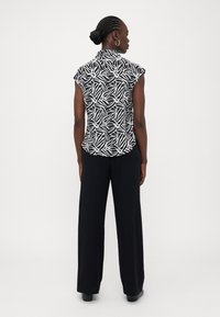 Μπλούζα κοντό μανίκι με μοτίβο ασπρόμαυρο και γιακά, συνδυασμένη με μαύρο παντελόνι φαρδύ. Μαλακό ύφασμα, εφαρμοστή σιλουέτα, ελάχιστα μεταλλικά αξεσουάρ.