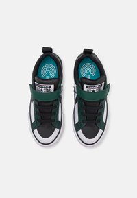 Zapatillas negras y verdes con suela blanca, diseño clásico de cordones, correa ajustable y plantilla en color teal con detalle de logo.