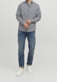 Camicia a righe blu e bianca, abbinata a jeans chiari strappati e sneaker bianche. Design semplice, vestibilità comoda.