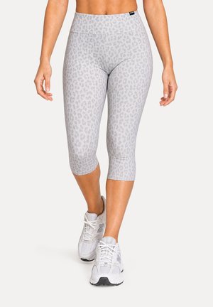 Femme portant des leggings capri gris clair à imprimé léopard et des chaussures de course blanches, debout avec un pied légèrement en avant.