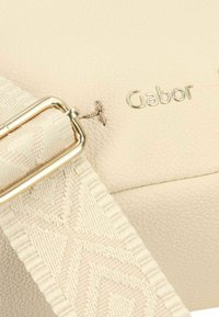 Bolso de cuero beige con superficie texturizada, que presenta una hebilla de metal en tono dorado y una correa de tela con patrón. Logo de Gabor grabado en dorado.