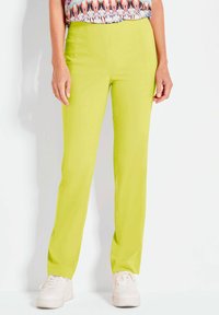 Limettengrüne Hosen mit einer glatten Textur und geradem Schnitt, ausgestattet mit vorderen Nähten und Seitentaschen, kombiniert mit weißen Sneakern.