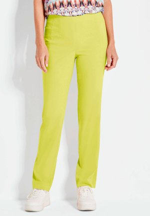 Limoengroene broek met een gladde textuur en rechte snit, voorzien van voornaad en zijzakken, gecombineerd met witte sneakers.