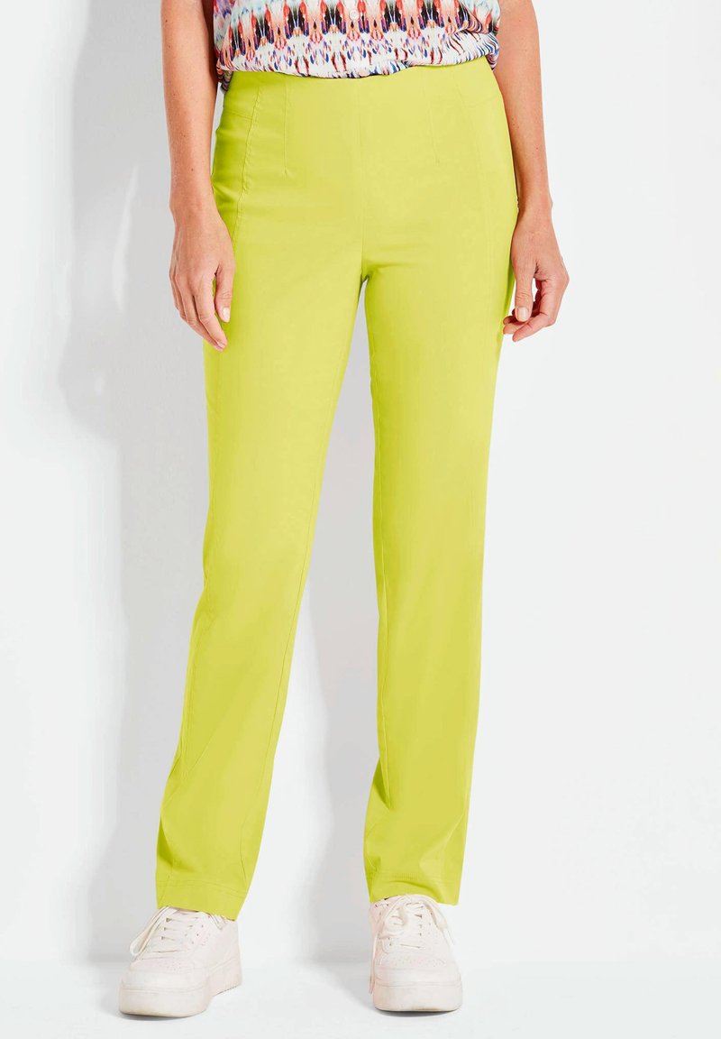 Limettengrüne Hosen mit einer glatten Textur und geradem Schnitt, ausgestattet mit vorderen Nähten und Seitentaschen, kombiniert mit weißen Sneakern.