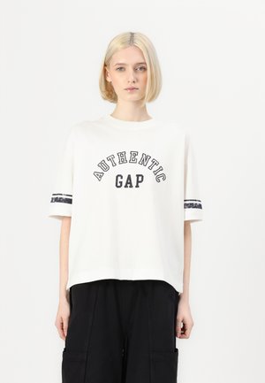 Bílý bavlněný tričko s černým nápisem "AUTHENTIC GAP", zdobené černobílými pruhovanými akcenty na rukávech. Volný střih, kulatý výstřih.