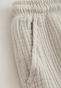 Světlé šedé texturované bavlněné kalhoty s elastickým pasem a bočními kapsami, s měkkým, mačkaným vzorem látky.