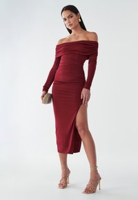 Burgundská šaty bez ramienok s dlhými rukávmi, priliehavý strih, nariasené tkanivo, bočný rozparok, v spojení so zlatými páskovými ihličkami a malou kabelkou.