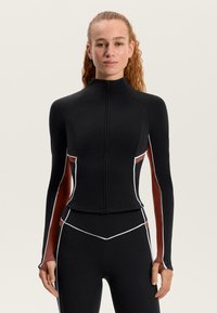 Schwarzes Langarmoberteil mit hohem Kragen, weißen Kontrastnähten und kontrastierenden rötlich-braunen Seitenpaneelen. Glatter, dehnbarer Stoff.