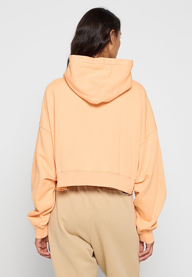Gekürzter Hoodie aus weichem Pfirsichstoff, mit großer Kapuze, weiten Ärmeln und geripptem Saum. Die Rückseite zeigt einen entspannten, übergroßen Schnitt.