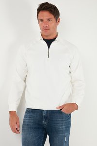 Valge poolkerge sviiter, millel on poolpikkus tõmblukk ja raglaansleevid, ning peene logo. Koos tumedate siniste teksadega, mis on mugava sobivusega.