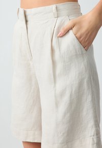 Shorts en lin de couleur beige clair avec une coupe décontractée, dotés de poches latérales et de plis subtils près de la taille.