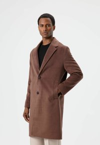 Bruine jas van wolmix met een reverskraag, twee knopen, zijzakken en een rechte snit. Zachte textuur en minimalistisch ontwerp.