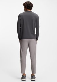 Langärmeliges graues Hemd kombiniert mit hellgrauen Jogginghosen, die eine lockere Passform und Taschen aufweisen. Dazu graue Sneaker getragen.