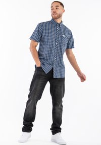 Short-sleeve blue checkered shirt with a buttoned collar and a chest pocket, paired with dark denim jeans and white sneakers.