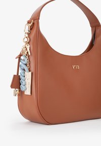 Bolso de hombro de cuero marrón con silueta curvada, herrajes dorados y charm decorativo con letras azules y un accesorio para llaves.