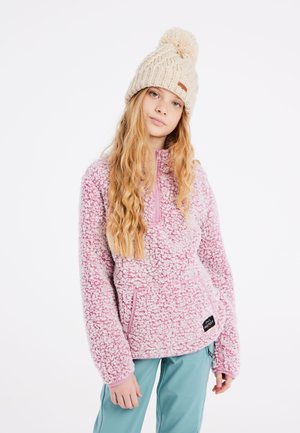 Pull en polaire rose avec col montant, manches longues et poches avant. Assorti à un pantalon bleu clair et à un bonnet en tricot beige avec un pompon.