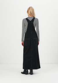 Musta farkkukangasta valmistettu overall-mekko, jossa on pitkä ja suora leikkaus, kahdella takataskulla ja säädettävillä olkaimilla. Yhdistetty pitkähihainen raidalliseen paitaan.