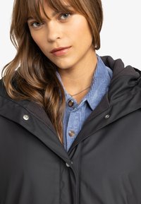 Zwarte hoodie jacket met een gestructureerde kraag, gelaagd over een lichtblauw corduroy shirt met knopen en een zachte afwerking.