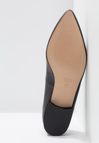 Černá kožená vysoká bota na jehlovém podpatku s špičatou špičkou a hladkým povrchem. Podešev je béžová s drážkovaným detailem, označená " vyrobeno ve Španělsku."