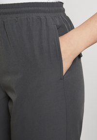 Harmaat joustavat vyötäröhousut sivutaskuilla, sileä rakenne, hyvin istuva malli ja näkyvä ommel yksityiskohtana taskujen ympäri.