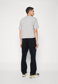 Grå kortærmet t-shirt kombineret med sorte cargo-bukser, der har cargo-lommer, samt matchende sorte og gule træningssko.