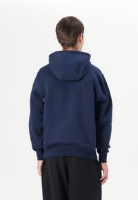 Sweatshirt com capuz azul marinho, com punhos e bainha canelados. Textura suave, capuz espaçoso e corte descontraído. Sem padrões ou acentos notáveis.