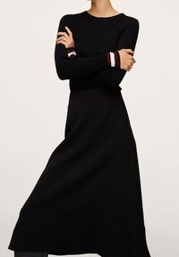 Haut noir à manches longues côtelé avec des accents rayés rouges et blancs au niveau des poignets, associé à une jupe noire fluide. Texture lisse, silhouette ajustée.