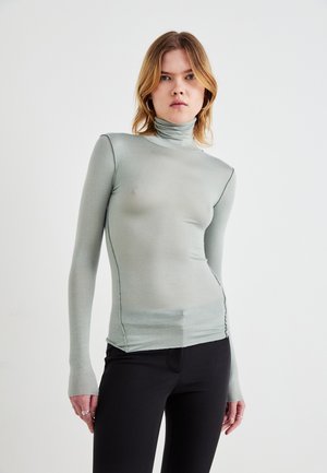 Pulover din tricot cu guler înalt, cu mânecă lungă, în nuanță de verde pal, realizat dintr-un material neted și elastic, cu laturi plisate și găuri pentru degete la capetele mânecii.