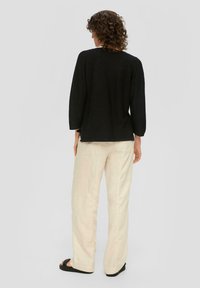 Schwarzer Strickpullover mit Dreiviertelärmeln, kombiniert mitcremefarbener Leinenhose. Das Outfit zeichnet sich durch eine lockere Passform und strukturierte Stoffe aus.
