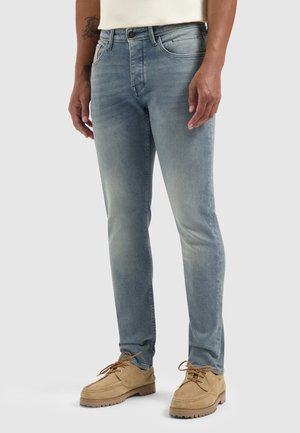 Lichtblauwe denim jeans met een slim fit, voorzien van een vervaging patroon, vijf zakken en een metalen knoopsluiting, gecombineerd met beige veterschoenen.