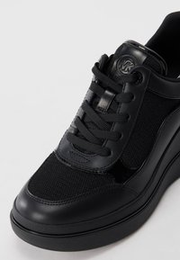 Černá teniska kombinující hladkou kůži a texturovanou síťovinu, ploché tkaničky a kulatý logotyp na jazyku.