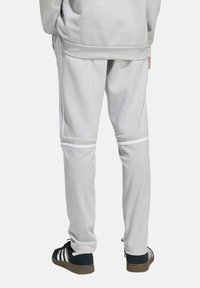 Hellgraue Sweatpants mit weißen Streifenakzenten, die eine entspannte Passform und ein weiches Material aufweisen. Der Saum hat einen gerippten Abschluss für zusätzlichen Komfort.