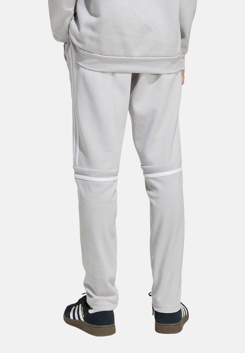 Hellgraue Sweatpants mit weißen Streifenakzenten, die eine entspannte Passform und ein weiches Material aufweisen. Der Saum hat einen gerippten Abschluss für zusätzlichen Komfort.