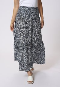Jupe longue et fluide avec un motif abstrait bleu marine et blanc, taille smockée et poches latérales. Associée à des chaussures blanches à enfiler.