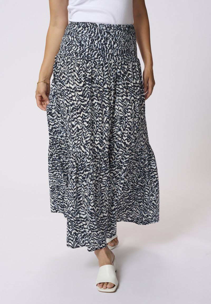 Jupe longue et fluide avec un motif abstrait bleu marine et blanc, taille smockée et poches latérales. Associée à des chaussures blanches à enfiler.