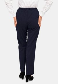 Marineblauwe, gestreepte broek met een elastische tailleband, gezien van achteren. Gepaarde met zwarte hoge hakken.