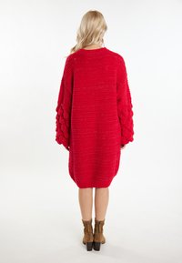 Abito maglione rosso oversize lavorato a maglia con maniche a sbuffo testurizzate; orlo a coste. Sotto, sono indicate stivali alla caviglia marroni con cerniere laterali.