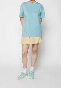 Jasnoniebieski bawełniany t-shirt z krótkimi rękawami i okrągłym dekoltem, zestawiony z beżową plisowaną spódnicą i miętowozielonymi trampkami.