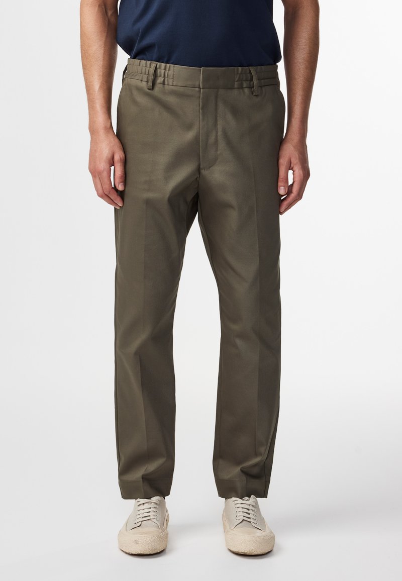 Olivengroene broek met een recht model; voorzien van een gestructureerde stof, een elastische tailleband en zijzakken, gecombineerd met beige schoenen.