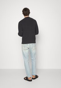 Jersey de marina, jeans de mezclilla claros y sandalias negras con acentos naranjas. Textura lisa, corte regular. Diseño sencillo sin patrones.