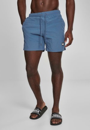 Blaue Badehosen aus leichtem Material, mit einem elastischen Bund und Kordelzug sowie einem seitlichen Logo-Patch. Strukturierte Oberfläche.