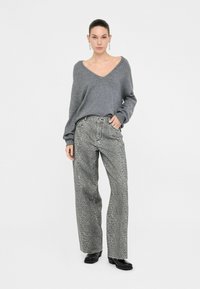 Pull en tricot gris avec un décolleté en V associé à un jean gris taille haute ample, comportant un subtil imprimé animal et un ourlet effiloché.
