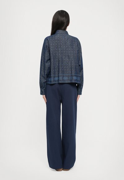 Navy blue cropped jacket with intricate light blue patterns, paired with wide-leg navy pants. Fabric appears woven with a textured finish.
