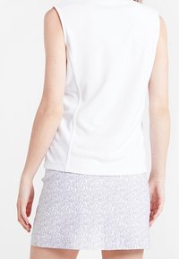 Bílý top bez rukávů z texturované látky spárovaný se světle fialovou vzorovanou sukní s květinovým motivem.