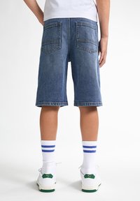 Jeansshorts i medelblått med en klassisk stil, som har två bakfickor och en rå nederkant, i kombination med vita strumpor och sneakers.