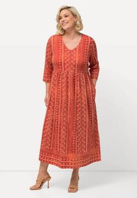 Vestido maxi rojo con escote en V, mangas tres cuartos y falda acampanada que presenta intrincados patrones florales y bolsillos. Textura de tela suave.
