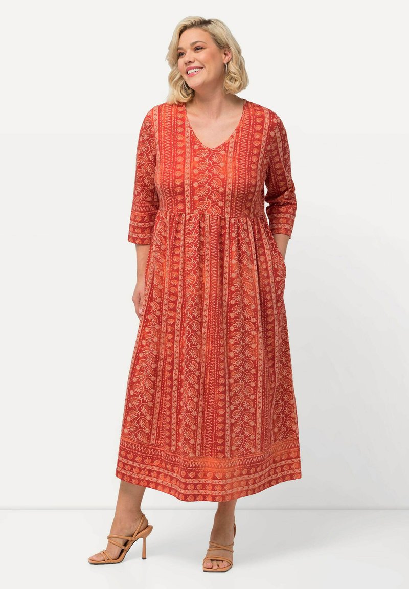 Vestido maxi rojo con escote en V, mangas tres cuartos y falda acampanada que presenta intrincados patrones florales y bolsillos. Textura de tela suave.