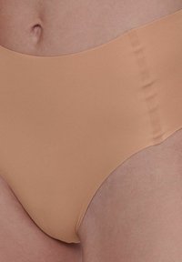 Beige hochgeschnittene Unterwäsche aus weichem, glattem Stoff mit Seitennähten und minimalistischem Design. Keine Muster, mit einfacher Verarbeitung.