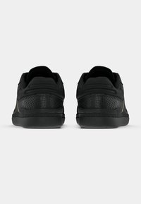 Black sneakers with a textured back, smooth upper, and subtle gold accents. Features a rounded shape and low-profile design with a rubber sole.