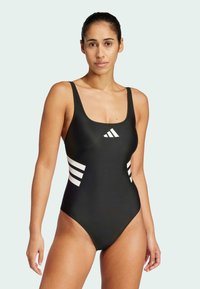 Maillot de bain une pièce noir avec un décolleté carré et des accents blancs à trois rayures sur les côtés. Tissu lisse et élastique avec un design ajusté.
